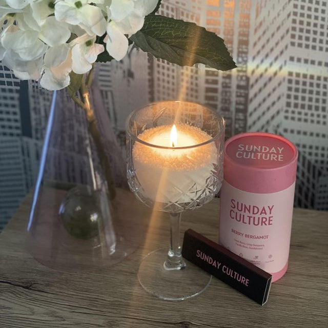 Candle, vase with flowers, and 'Sunday Culture' products on a wooden surface.