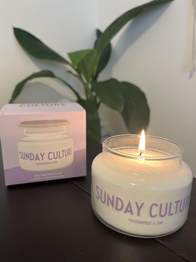 Sunday Culture scented candle with next to a plant and product packaging.