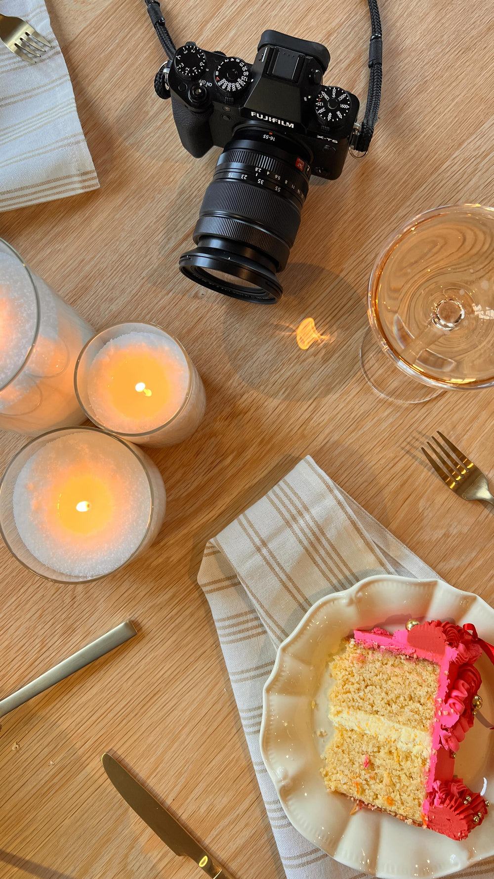 Camera on a wooden table with sand wax candles, a plate of cake, and a glass.