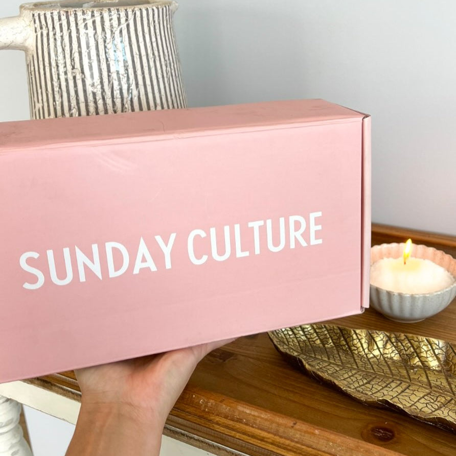 Sunday Culture pink bundle box held by a hand on a wooden surface.